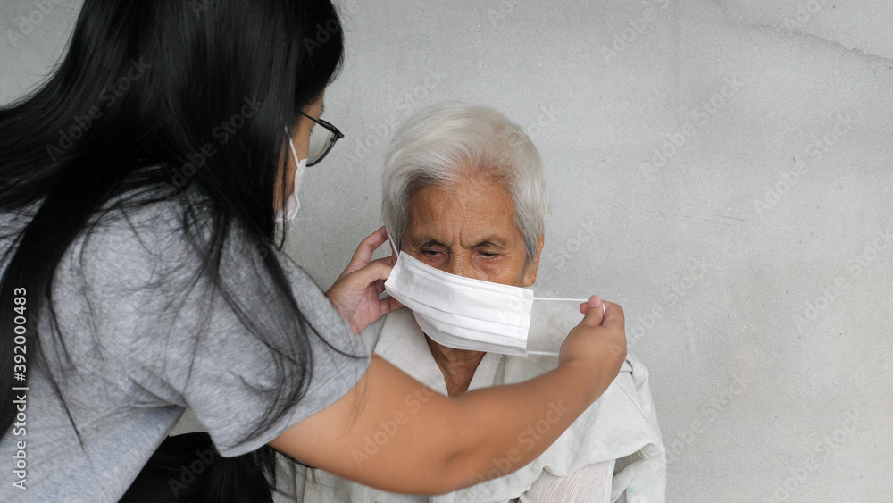 Asian grandchild woman wearing a white face mask to old grandmother prevent from covid 19. isolated concrete grey wall background. Rural lifestyle and health care concept.