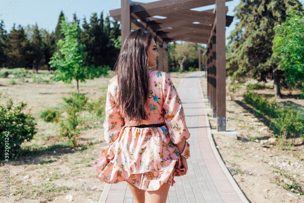 Obraz premium Beautiful fashionable brunette woman in a dress with flowers walks in the park on the street