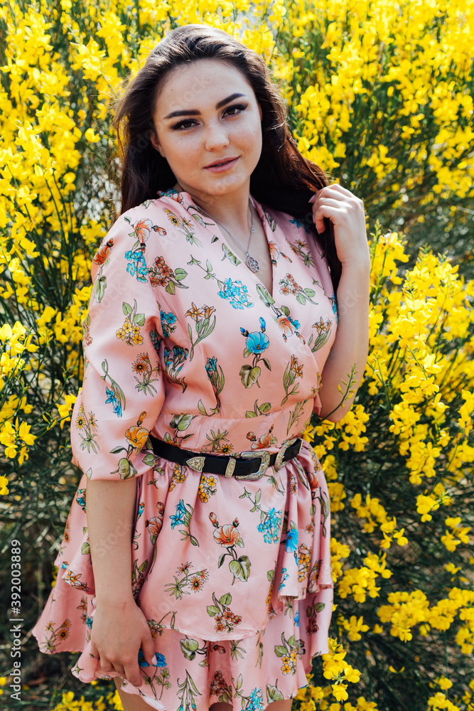 beautiful woman in a dress with flowers near the bushes of yellow flowers