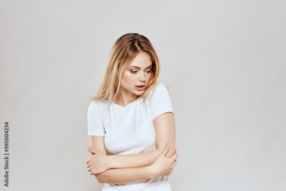 Obraz premium cheerful blonde in a white t-shirt gesturing with her hands light background