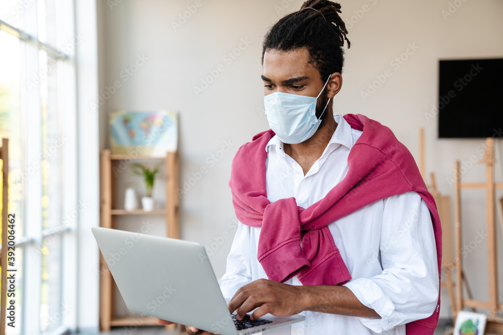 Focused african american guy in face mask using laptop Focused african american guy in face mask using laptop