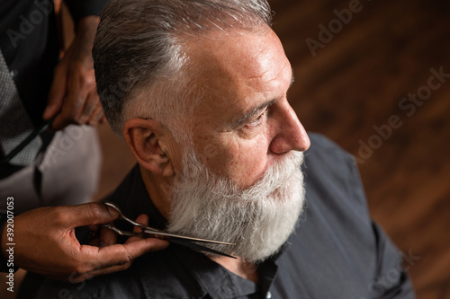 barber cuts the beard to the customer with the scissors.