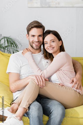 cheerful man and woman hugging while sitting on sofa at home