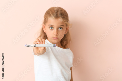Little diabetic girl with insulin syringe on color background