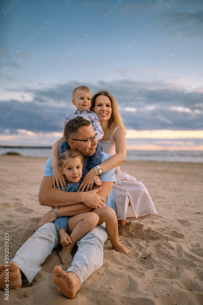 young parents and children, boy and a girl sitting on the sand on the beach and hugging each other. Image with selective focus.