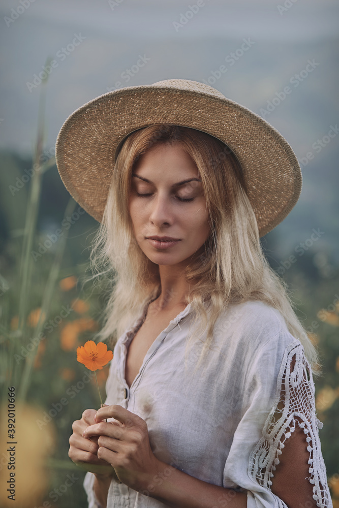 The blonde in a linen dress walks among herbs and wildflowers on a meadow in the mountains. A woman in the Boho style, resting in the countryside, a simple village lifestyle