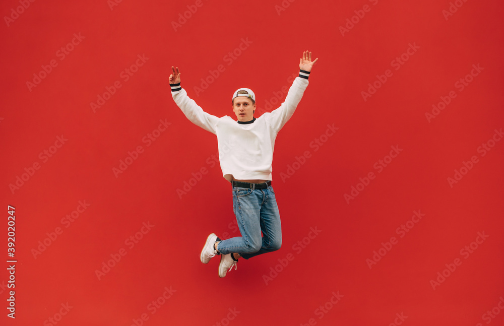 Stylish young man in casual clothes in a jump on a background of a red wall, looking at the camera with a serious face. Isolated. Stylish young man in casual clothes in a jump on a background of a red wall, looking at the camera with a serious face. Isolated.