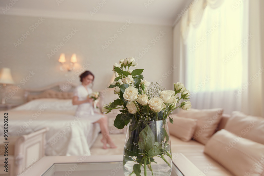 A girl in a white negligee is sitting on the bed with a bouquet of white roses in her hand A girl in a white negligee is sitting on the bed with a bouquet of white roses in her hand
