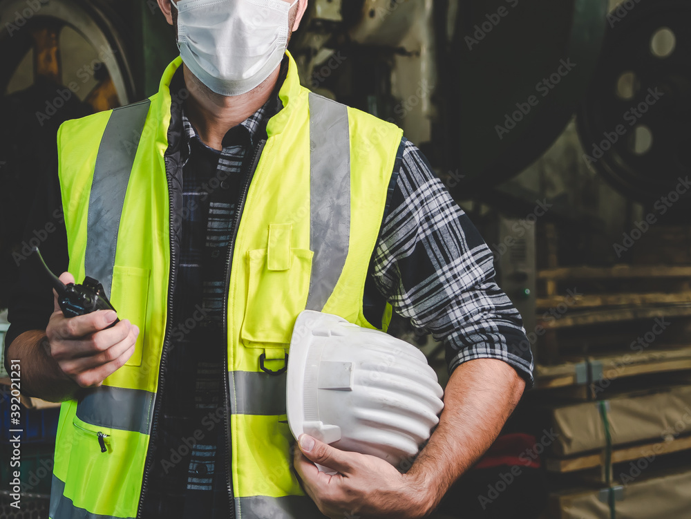 A factory worker holds a hard hat and talks a radio A factory worker holds a hard hat and talks a radio