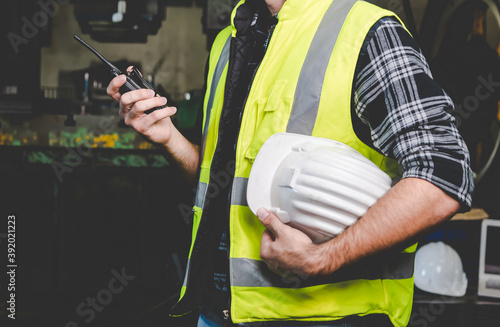 A factory worker holds a hard hat and talks a radio