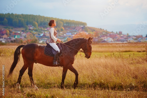 Beautiful young woman riding a horse in a field. Sideways to the camera. Freedom, joy, movement