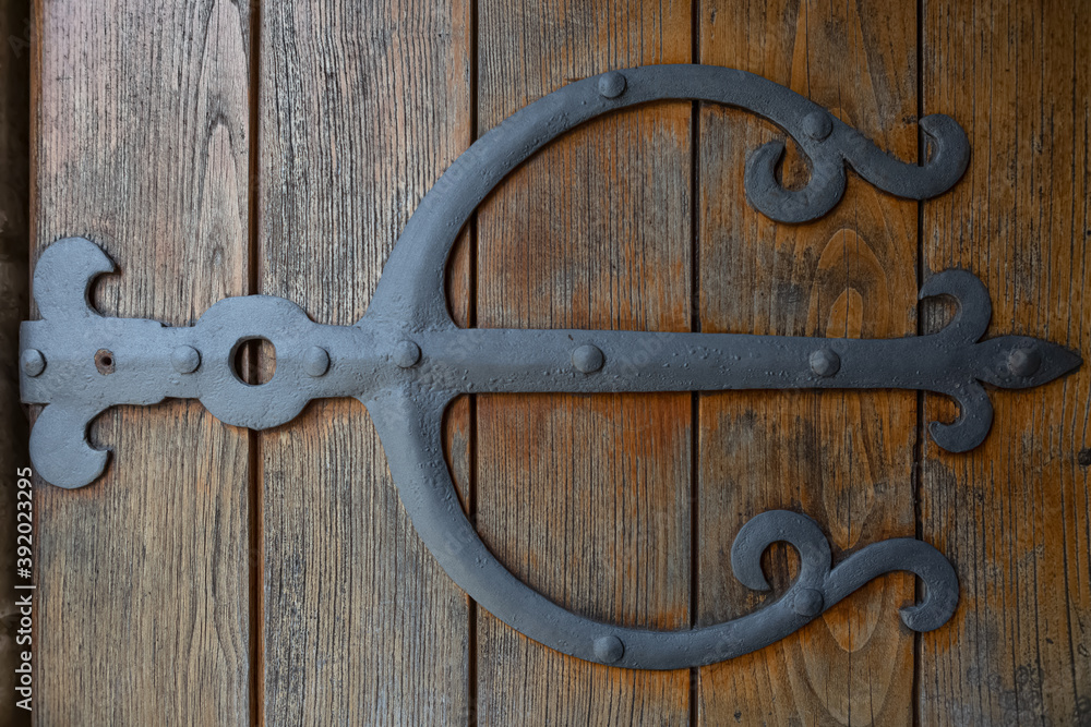Detail view of medieval metallic ornate hinge on rustic wooden door Detail view of medieval metallic ornate hinge on rustic wooden door