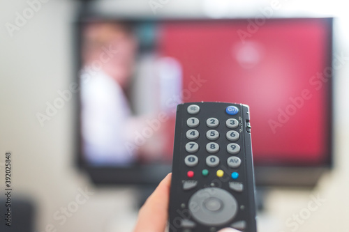 Male hand is holding TV remote control, streaming on a smart TV.