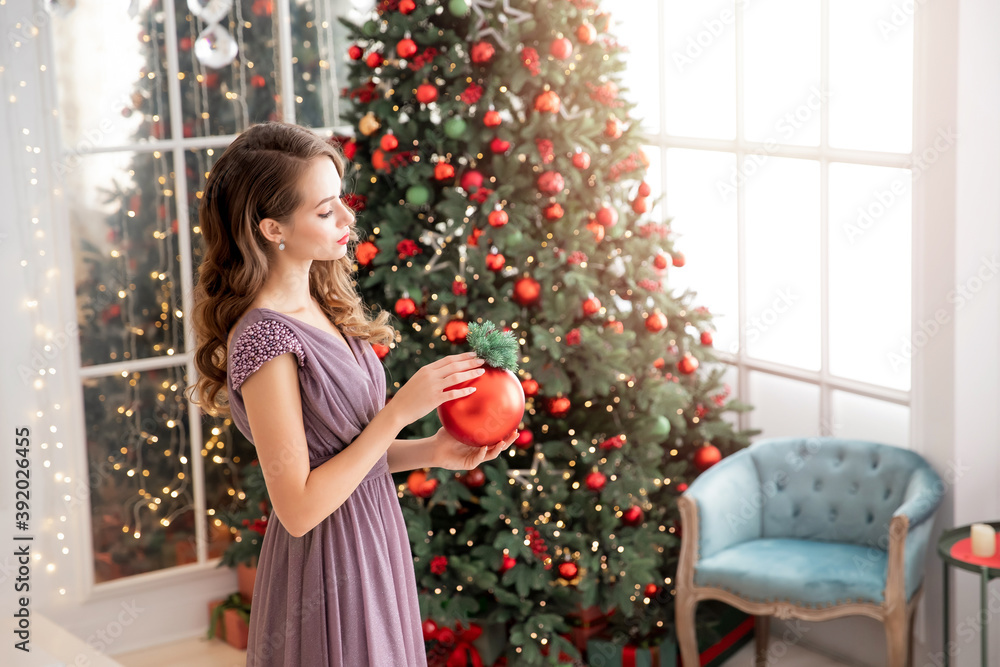 Young woman with make-up and hairstyle holds gift balls for decor of Christmas tree. Concept preparation for holidays New Year