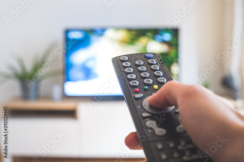 Male hand is holding TV remote control, streaming on a smart TV.