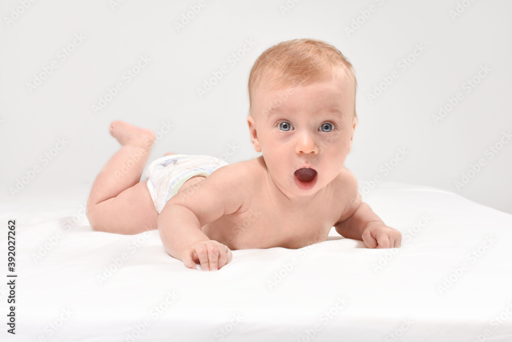 Adorable, amazed, caucasian baby girl or boy lying on stomach, on white blanket looking at camera, on white background. Open mouth, healthy skin. Baby care concept. Adorable, amazed, caucasian baby girl or boy lying on stomach, on white blanket looking at camera, on white background. Open mouth, healthy skin. Baby care concept.