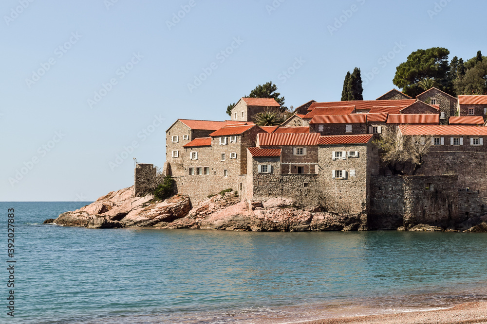 Sveti Stefan island seen from the beach. The day is beautiful and the sky is blue.