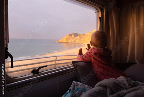 Baby looking from campervan window over the beach in the coastal town of Praia do Burgau, Portugal. photo