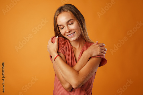 Peaceful young blonde woman holding hands on her chest.