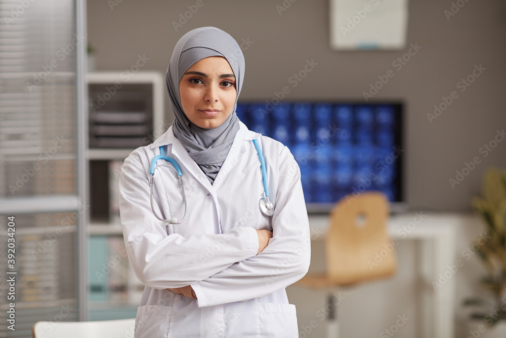 Portrait of muslim doctor in white coat standing with her arms crossed at hospital looking at camera