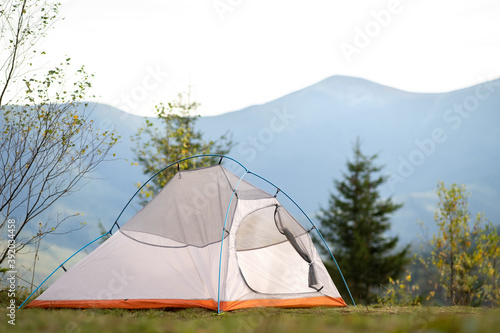 Empty hikers tent standing on campsite with view of majestic high mountain peaks in distance. Camping in wild nature and active travelling concept.