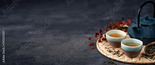 Green Tea Composition with blue teapot on dark background banner. Chinese traditional tea set, ceremony concept, selective focus, copy space.