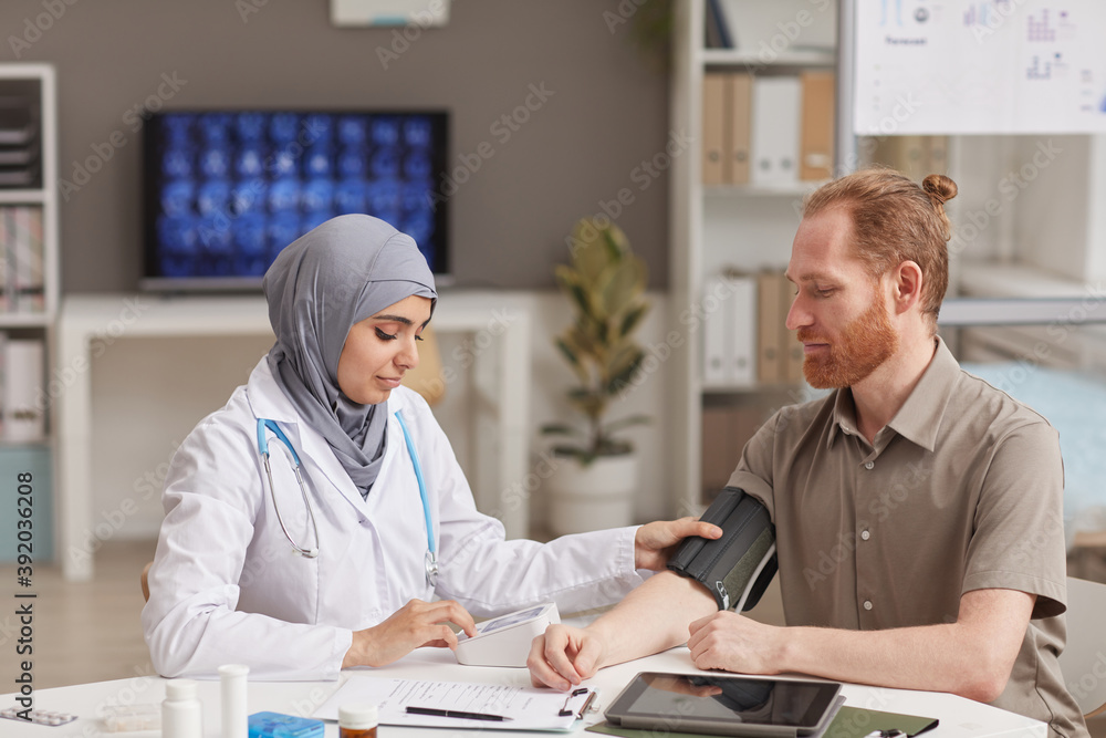 Φωτογραφία Muslim female doctor measuring the pressure of male patient during his visit at