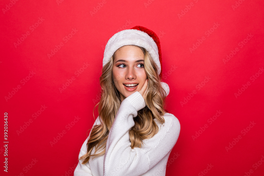 Young pretty woman in warm clothes in santa hat isolated on red background Young pretty woman in warm clothes in santa hat isolated on red background