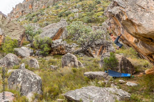 Athletic male climbs outside on a boulder in a grassy, rocky landscape photo