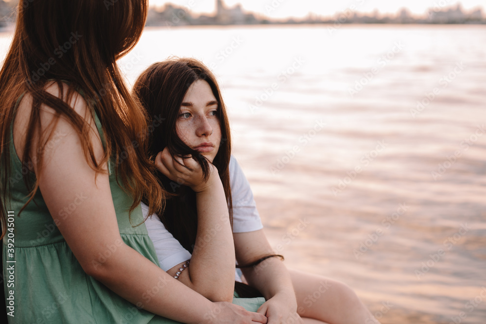 Thoughtful lesbian couple sitting by river in city at sunset Thoughtful lesbian couple sitting by river in city at sunset