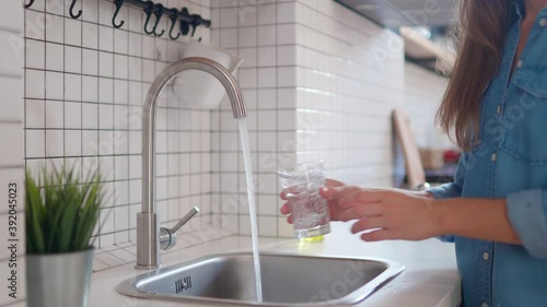 Woman pouring clean filtered water from the tap in glass for drinking at modern loft style kitchen