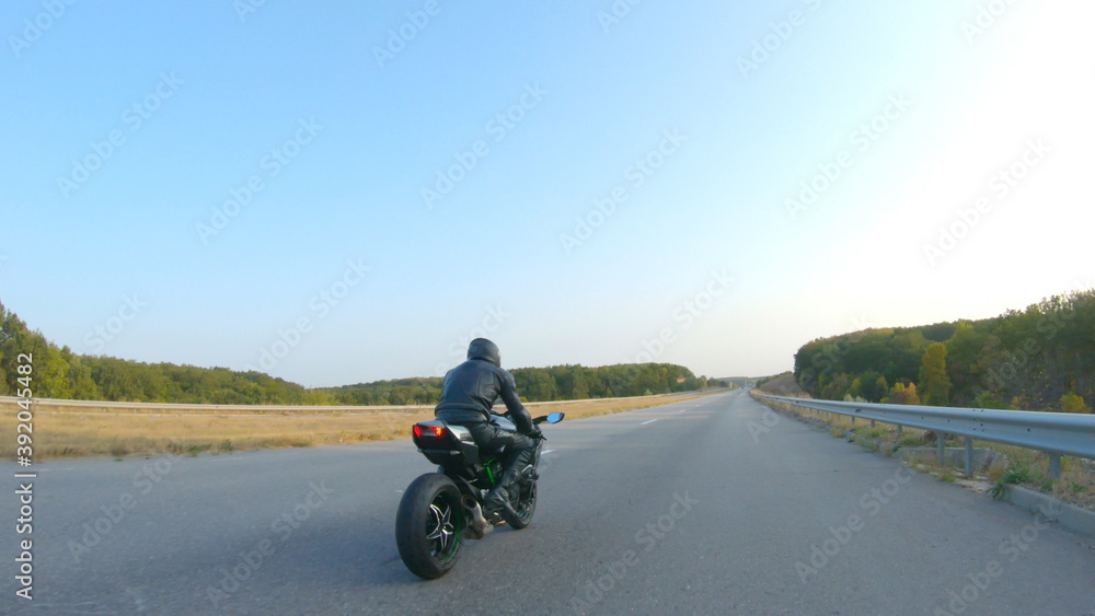 Follow to motorcyclist in helmet riding on sport motorbike at highway. Man racing his motorcycle on autumnal country road. Guy driving bike during trip. Concept of freedom and adventure. Aerial shot Follow to motorcyclist in helmet riding on sport motorbike at highway. Man racing his motorcycle on autumnal country road. Guy driving bike during trip. Concept of freedom and adventure. Aerial shot