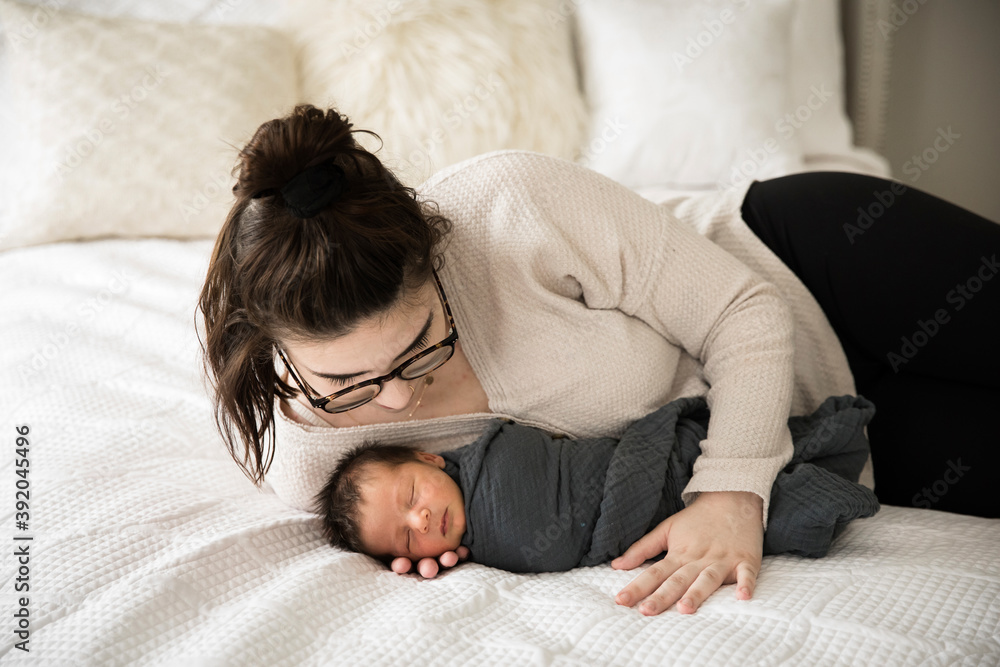 Hipster Millennial Mom Snuggles Swaddled Newborn on White Bed Hipster Millennial Mom Snuggles Swaddled Newborn on White Bed