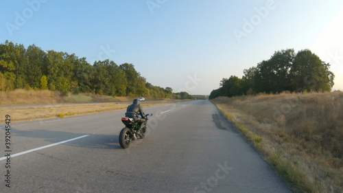 Follow to motorcyclist in helmet riding on sport motorbike at highway. Man racing his motorcycle on autumnal country road. Guy driving bike during trip. Concept of freedom and adventure. Aerial shot