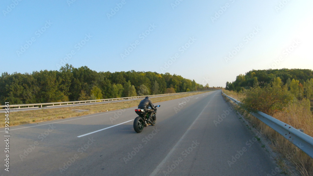 Follow to biker riding on modern sport motorbike at highway during sunny autumn day. Motorcyclist racing his motorcycle on country road. Guy drive bike during trip. Concept of journey. Aerial shot