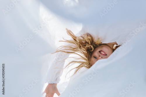 village child with blond hair tangled among the washed laundry