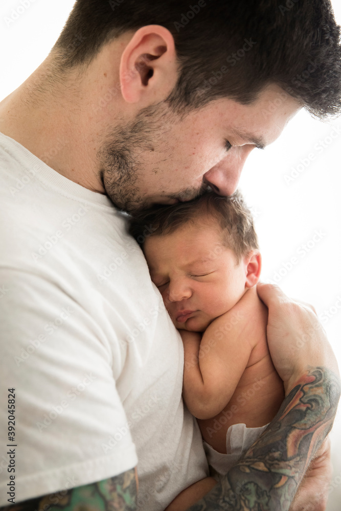 Close Up Side View of Tattooed Millennial Dad Kissing Newborn Son Close Up Side View of Tattooed Millennial Dad Kissing Newborn Son