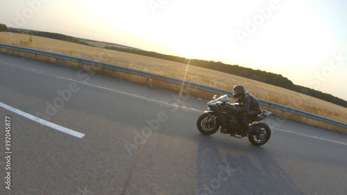 Camera moving around of biker riding on modern sport motorbike at highway. Motorcyclist racing his motorcycle on country road at sunset. Man driving bike during trip. Concept of freedom and adventure