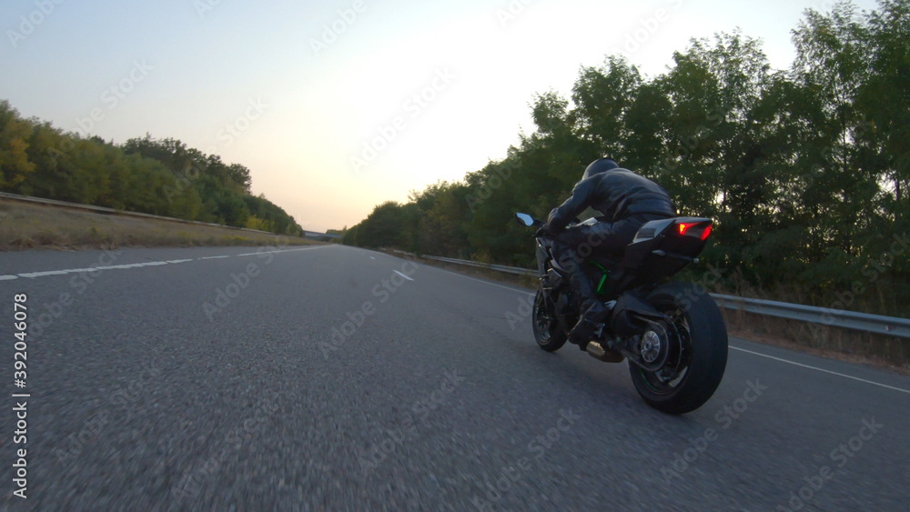 Obraz premium Biker is accelerating at motorcycle on empty country road. Man riding fast on modern sport motorbike at autumn highway. Guy driving bike during trip. Concept of freedom and adventure. Aerial shot