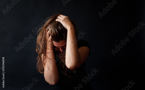 Distressed woman with long brown hair holding her head in her hands.