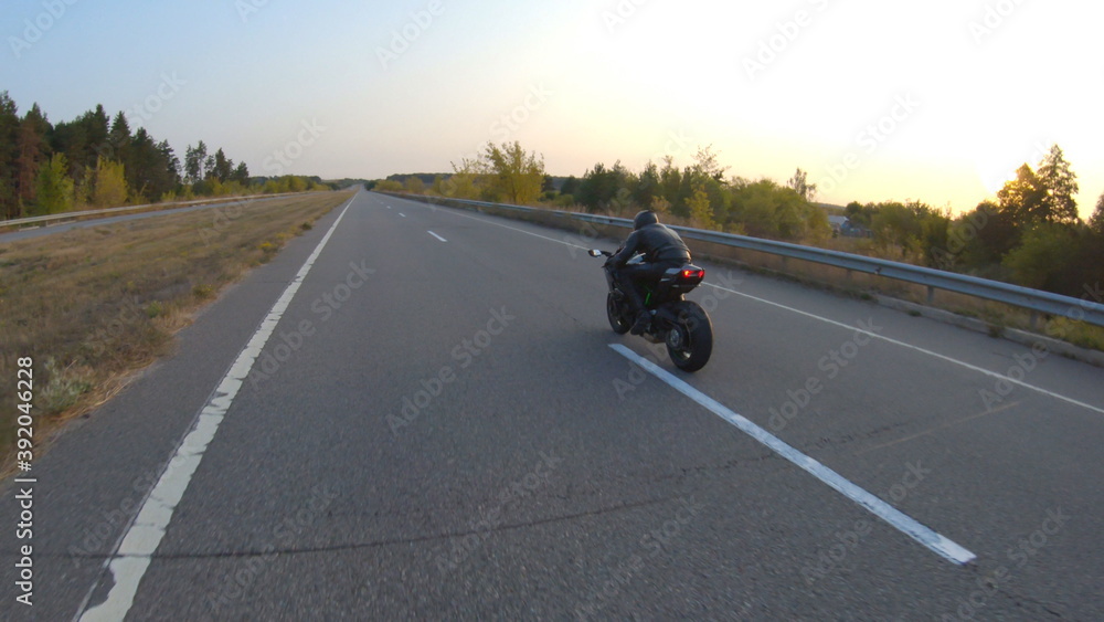 Follow to biker riding on modern sport motorbike on country road at sunset. Motorcyclist racing his motorcycle at highway. Guy driving bike during trip. Concept of journey and freedom. Aerial shot