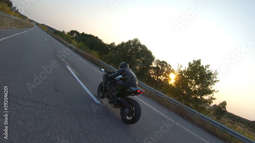 Follow to biker riding on modern sport motorbike on country road at sunset. Motorcyclist racing his motorcycle at highway. Guy driving bike during trip. Concept of journey and freedom. Aerial shot