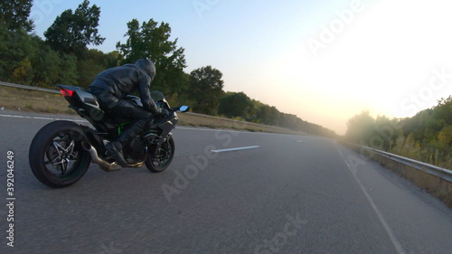 Camera moving around of biker riding on modern sport motorbike at highway. Motorcyclist racing his motorcycle on country road at sunset. Man driving bike during trip. Concept of freedom and adventure © olehslepchenko