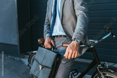 Cropped view of businessman in suit holding briefcase near bicycle outdoors