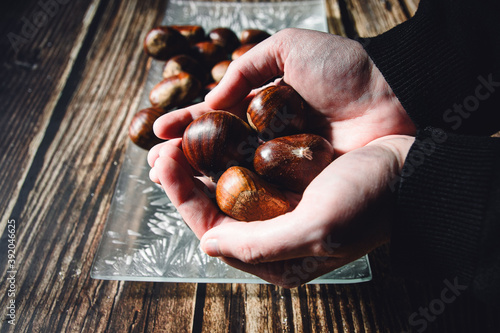 Hands of a woman holding various chestnuts. In the background a plate