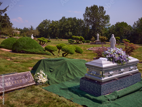 A casket with flowers sits beside a gravesite ready for burial.