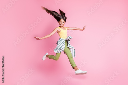 Full length photo of cheerful shiny child girl dressed casual outfit jumping hands arms sides isolated pastel pink color background © deagreez