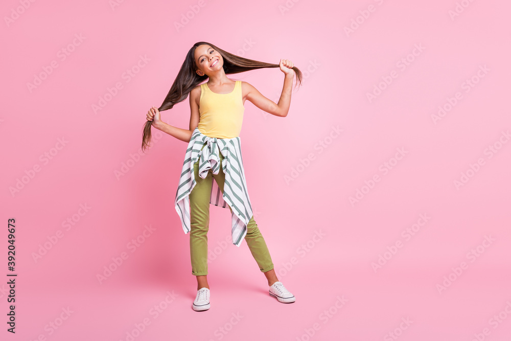 Full length photo of happy cheerful little girl hold hair wear green pants isolated on pastel pink color background