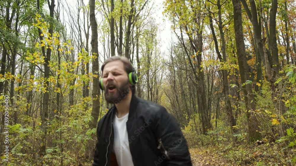 A young brutal Caucasian man is emotionally walking in an autumn park and listening to music on headphones. Dancing and relaxation A young brutal Caucasian man is emotionally walking in an autumn park and listening to music on headphones. Dancing and relaxation