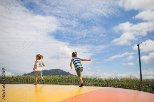 Boy and girl running on trampoline, outdoors in rural area.